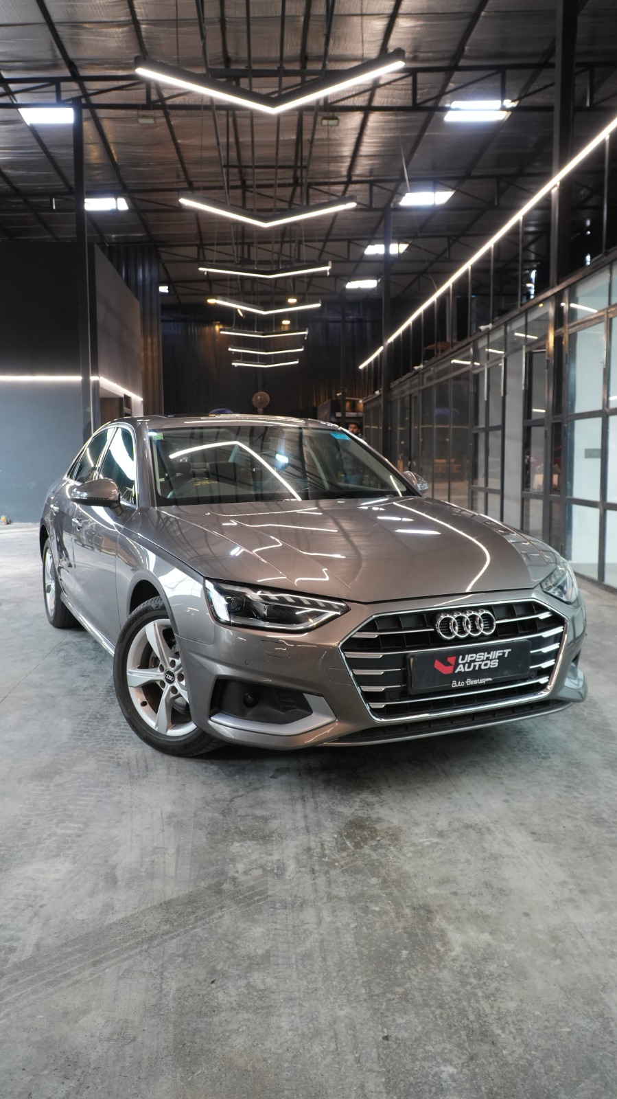 A grey Audi A4 saloon, front three-quarter view in the workshop hall beneath chevron strip lights.