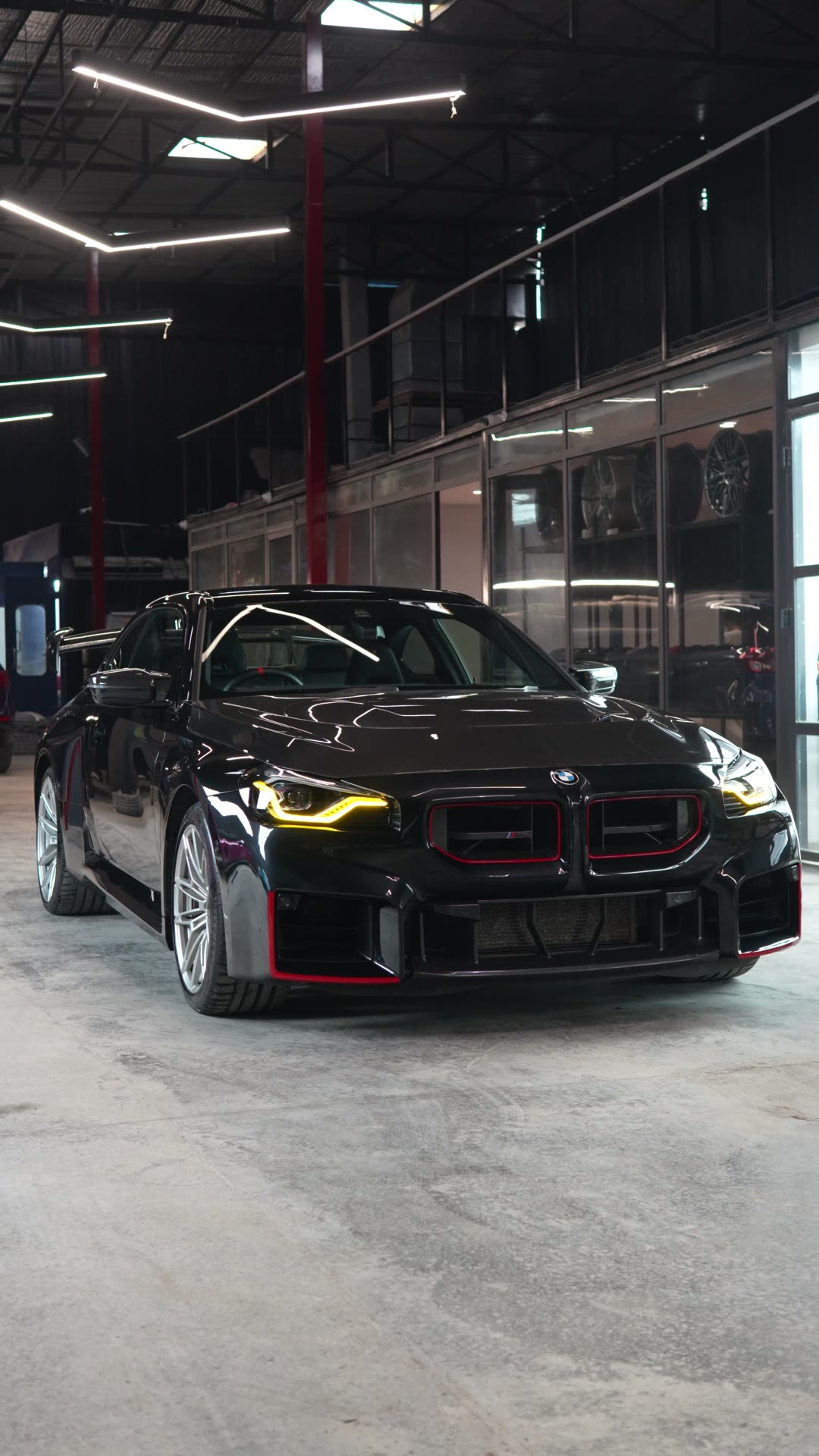 A black BMW M2 with red grille accents in the workshop hall