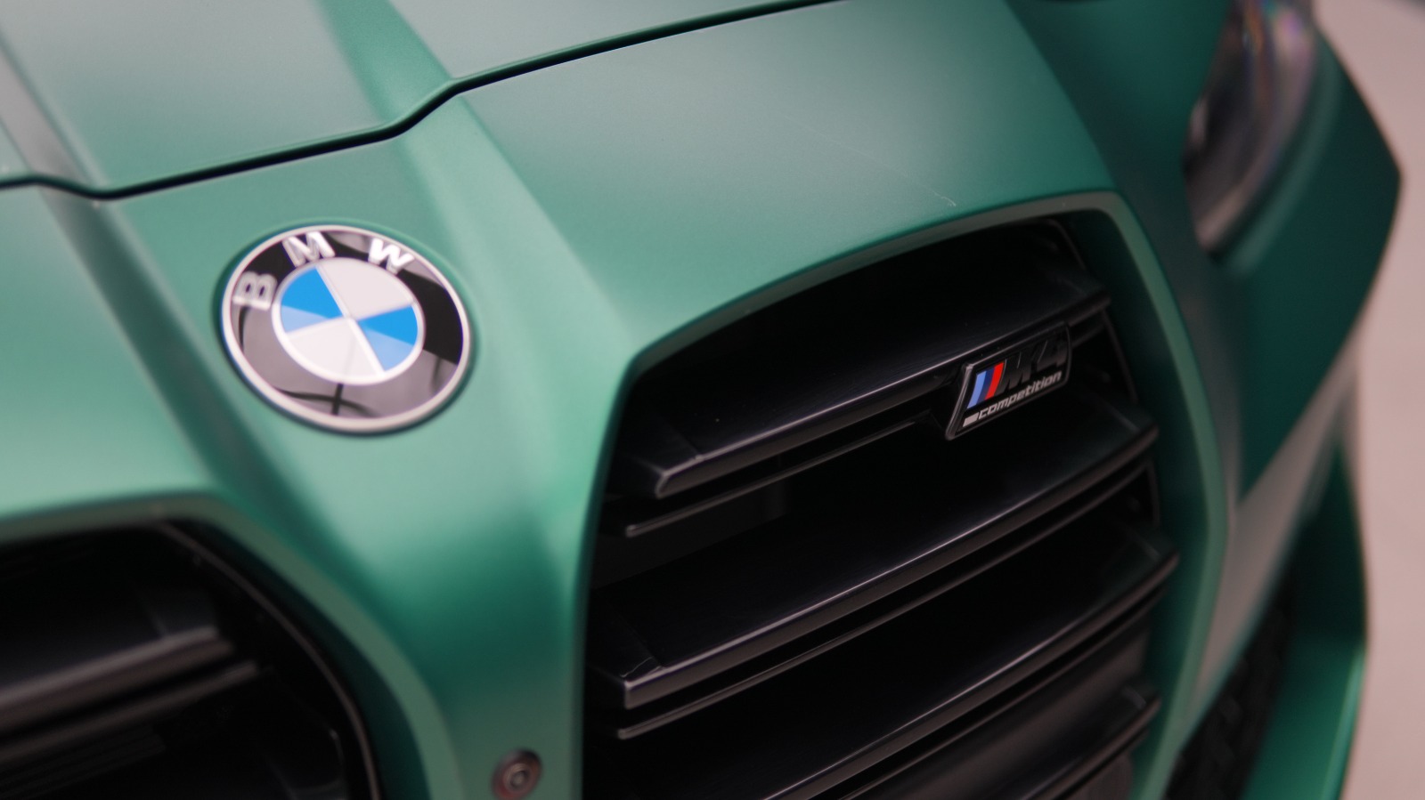 Close view of the satin green BMW M4's roundel and vertical kidney grille with its M badge.