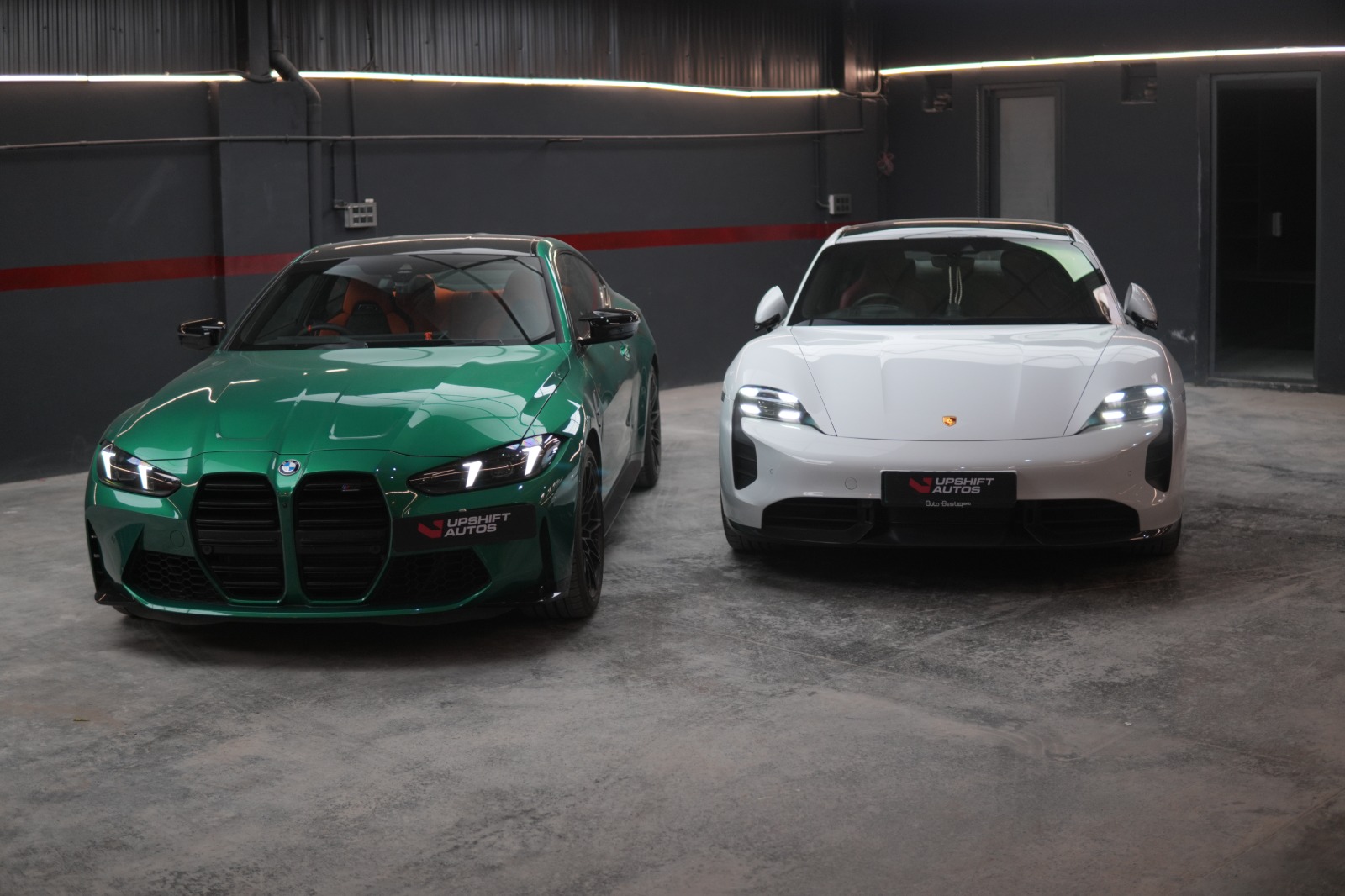 The satin green BMW M4 parked beside a white Porsche Taycan in the workshop.