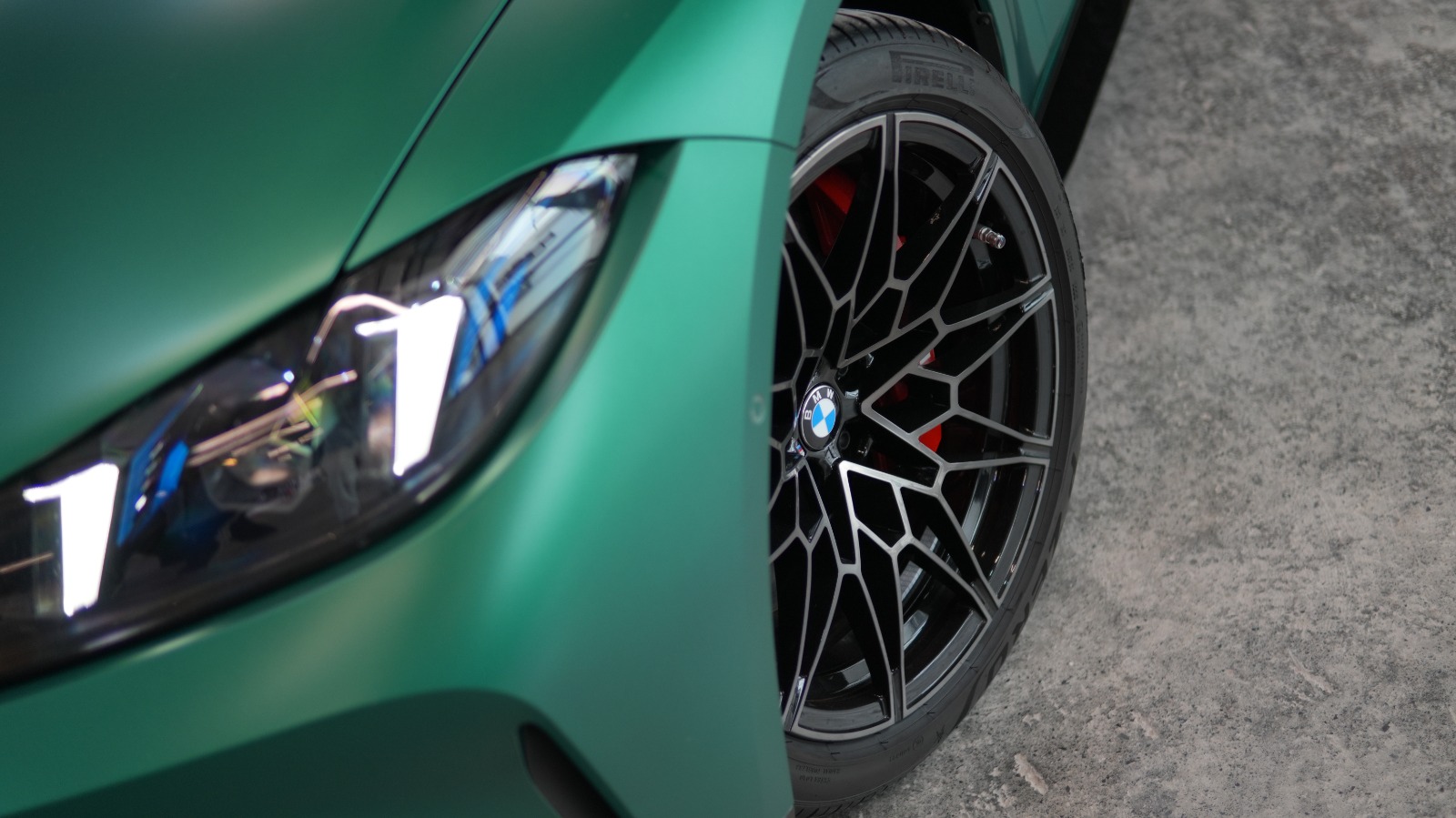 Close view of the satin green BMW M4's headlamp and black forged wheel with a red brake caliper.