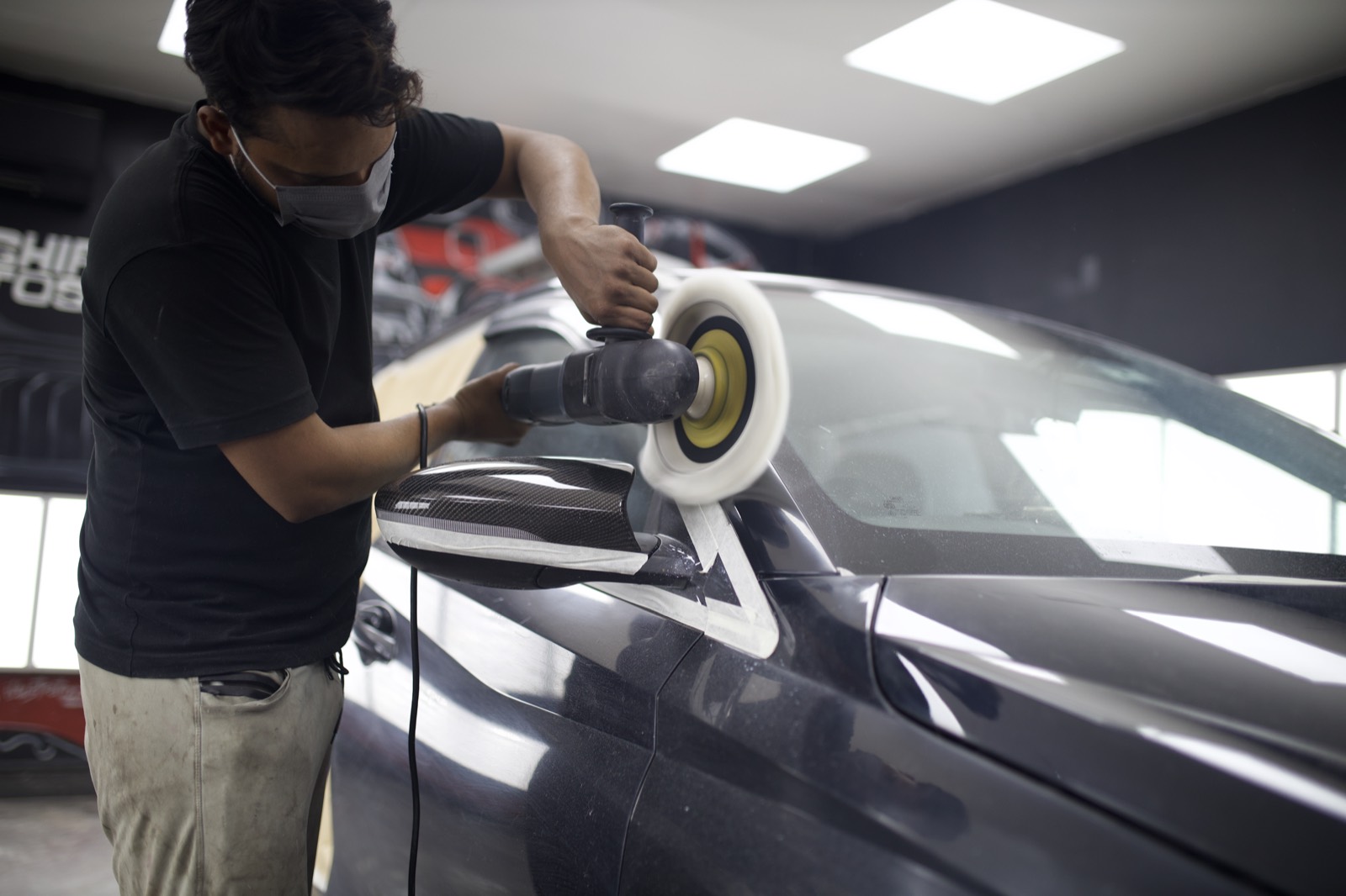 Machine polishing the paint on a dark grey car in the workshop