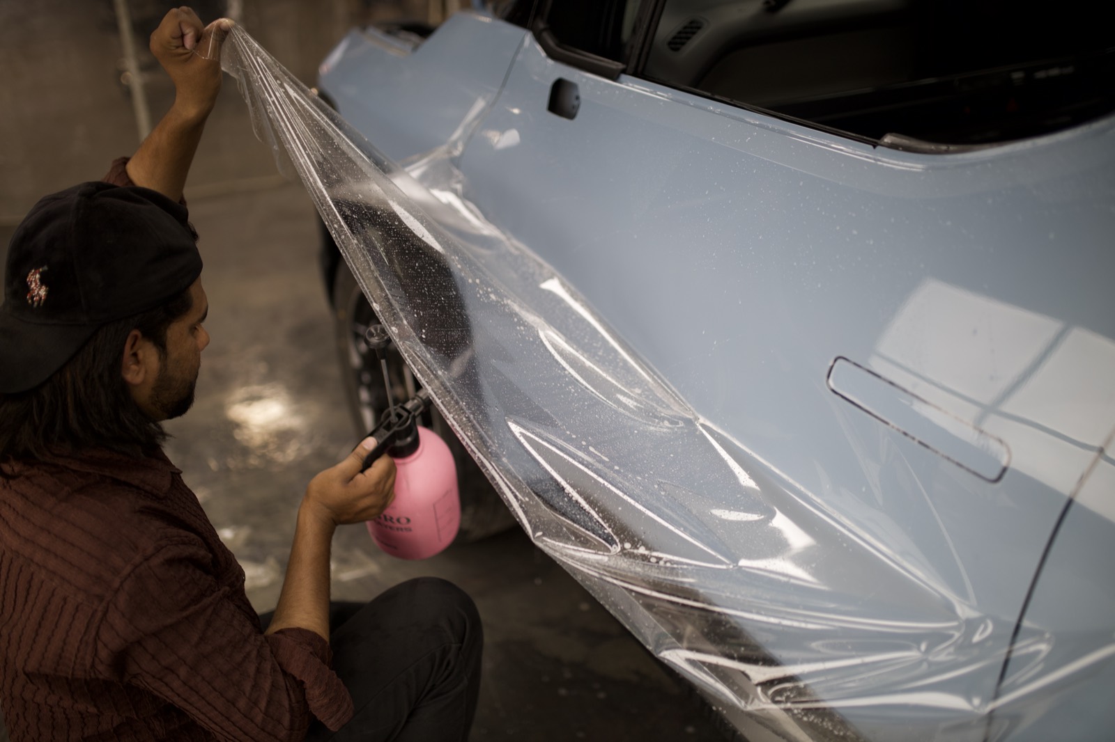 A sheet of clear paint protection film being laid over a car door