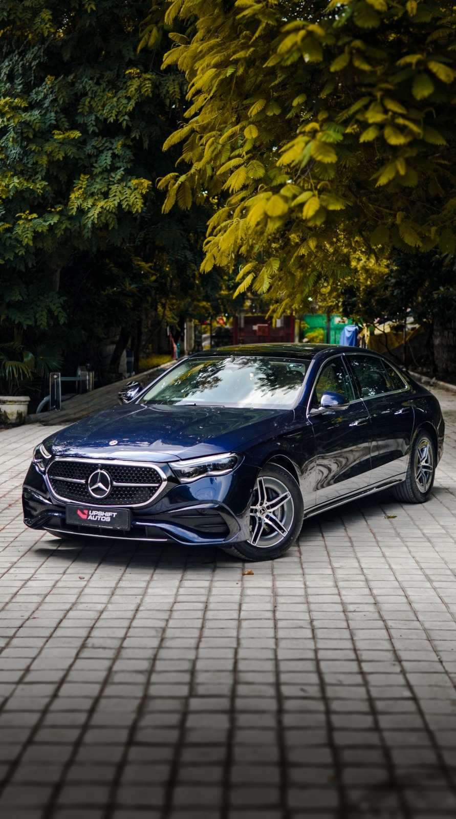 The dark blue Mercedes-Benz E450 on a paved courtyard under trees, front three-quarter view from the driver's side.