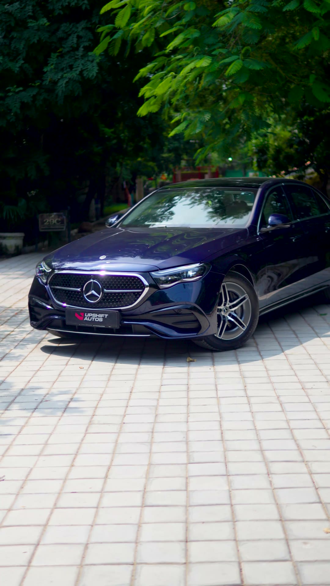 A dark blue Mercedes-Benz E450 parked outdoors on a paved drive under trees, front three-quarter view.