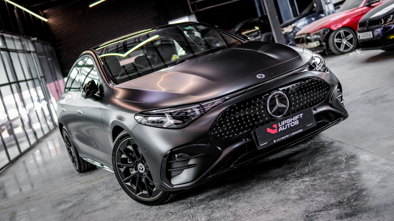 The matte grey EQE from a wider angle in the workshop, with other cars and parts behind it.