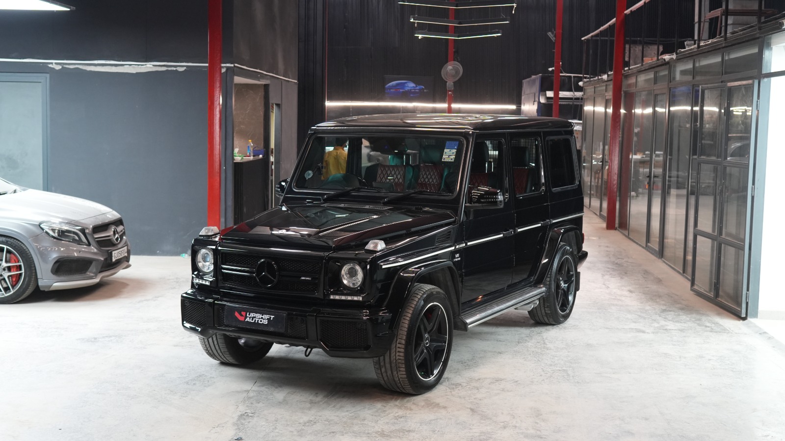 The black G63 head-on in the workshop hall, with a silver Mercedes saloon parked to one side.