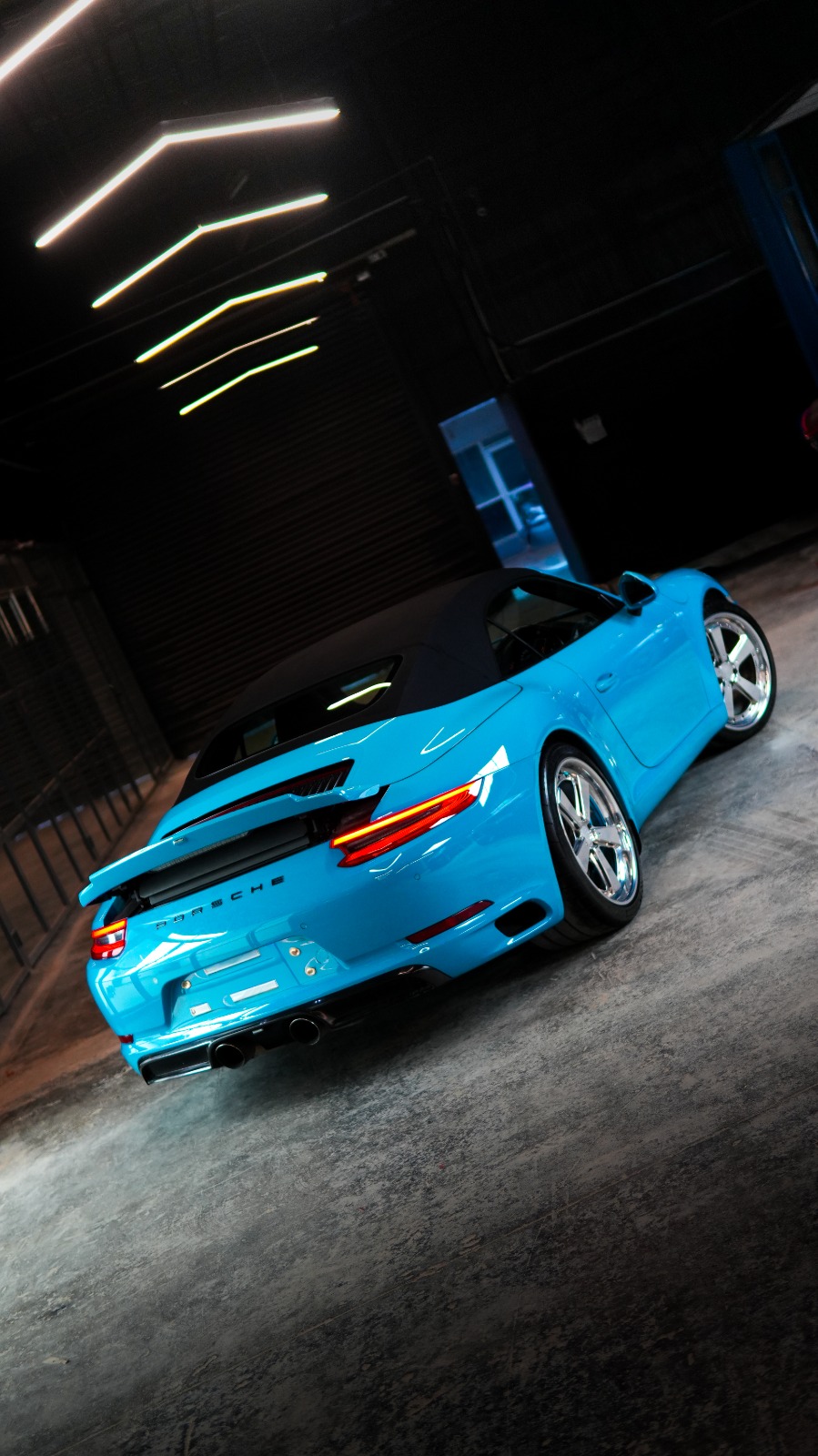 The blue Porsche 911 Cabriolet from a low rear angle, its full-width tail lamp lit.