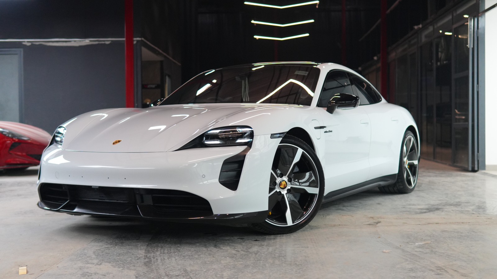 A white Porsche Taycan with black wheels, front three-quarter view in the workshop hall.