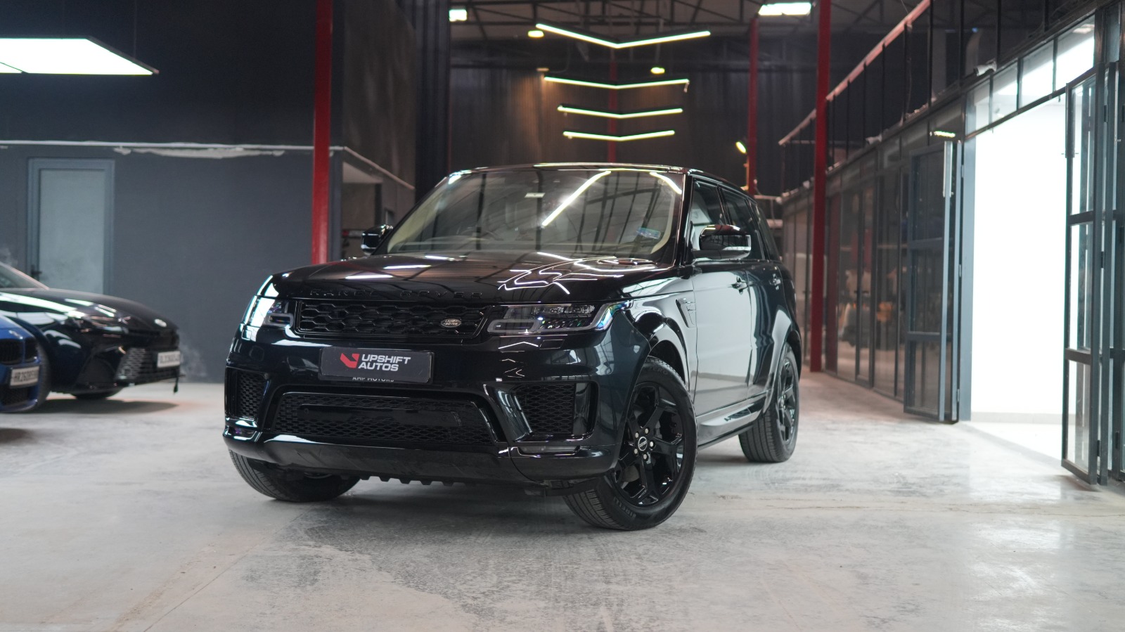 A black Range Rover Sport, front three-quarter view in the workshop hall with its doors open to daylight.