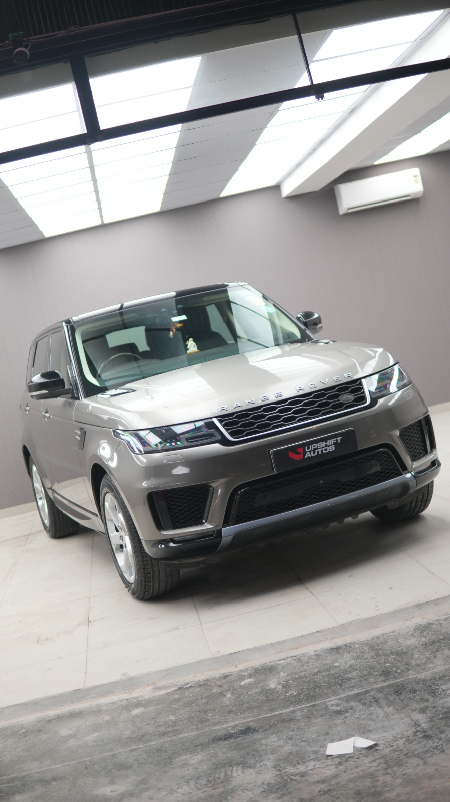 A grey Range Rover Sport, front three-quarter view in a white-walled bay.