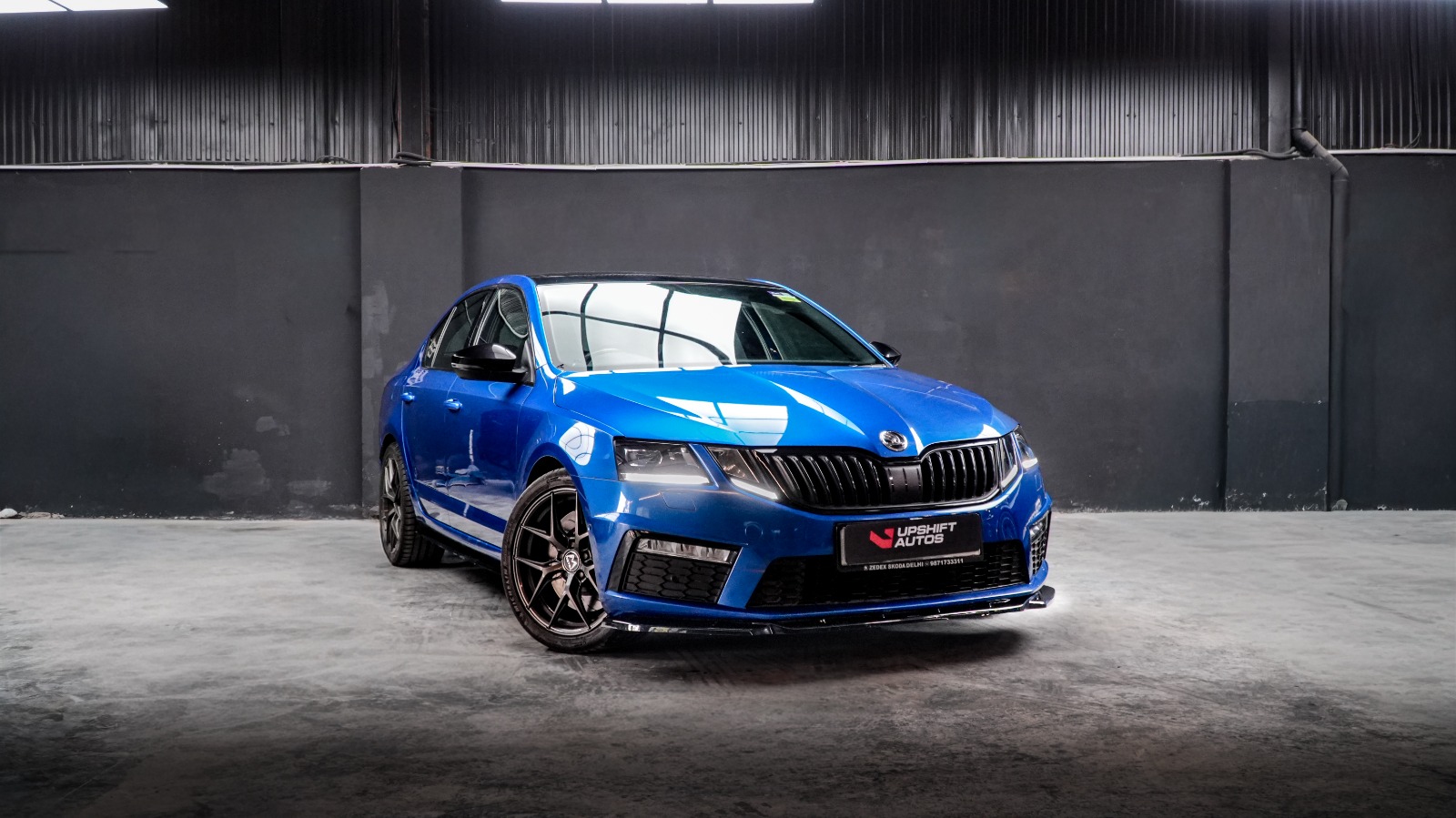 A blue Škoda Octavia vRS with bronze wheels, front three-quarter view against a dark workshop wall.