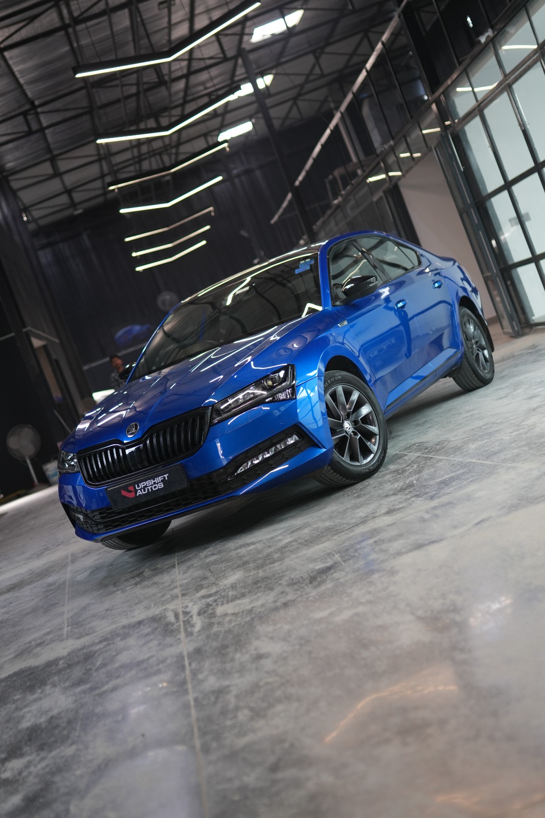 The blue Škoda Superb from a low front angle on the polished workshop floor.