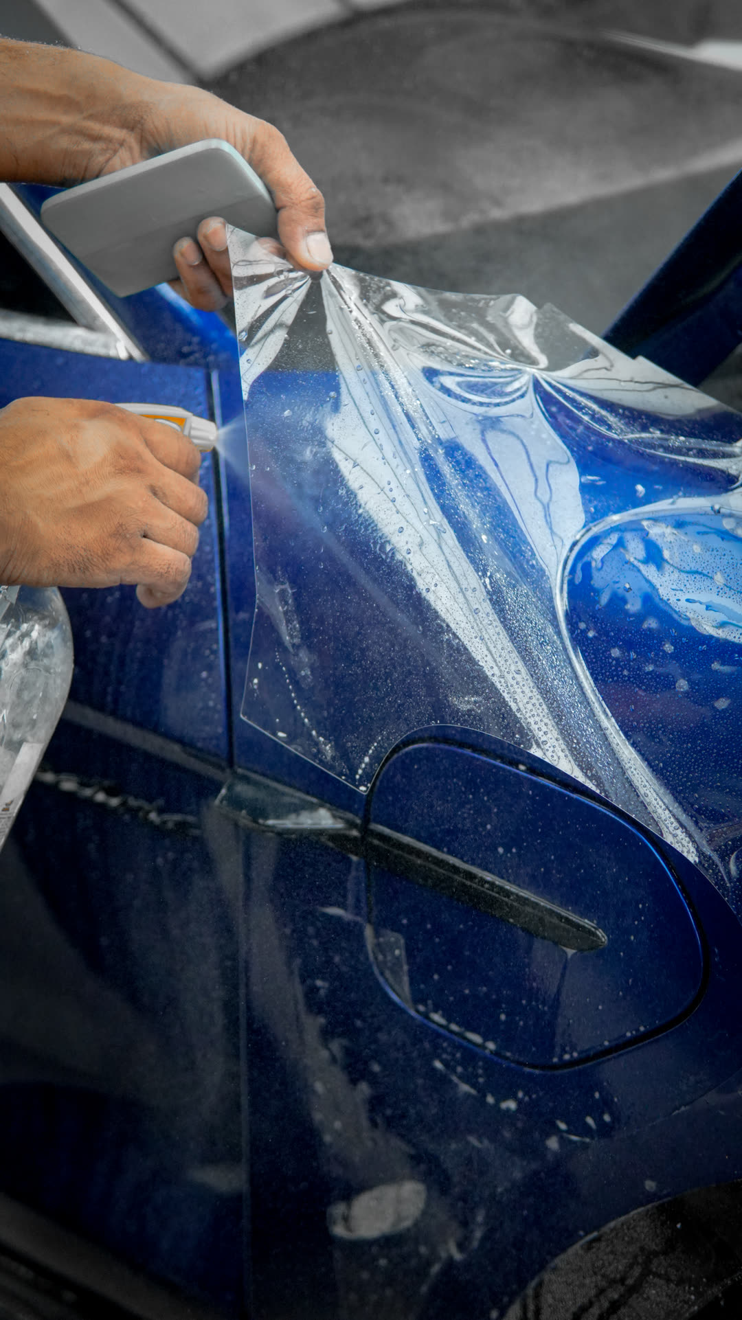 Clear paint protection film being squeegeed onto the door of a blue Porsche Taycan