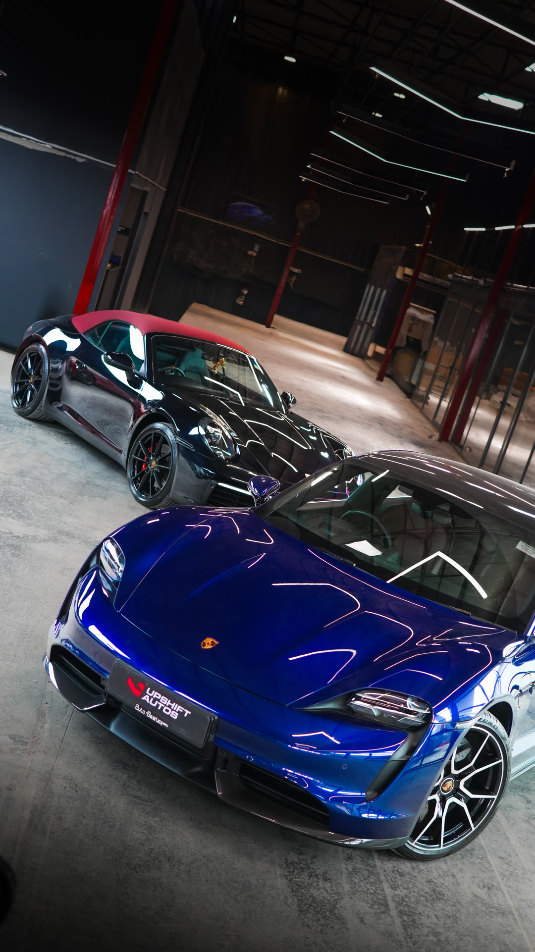 A blue Porsche Taycan beside a second Porsche in the Upshift Autos workshop hall