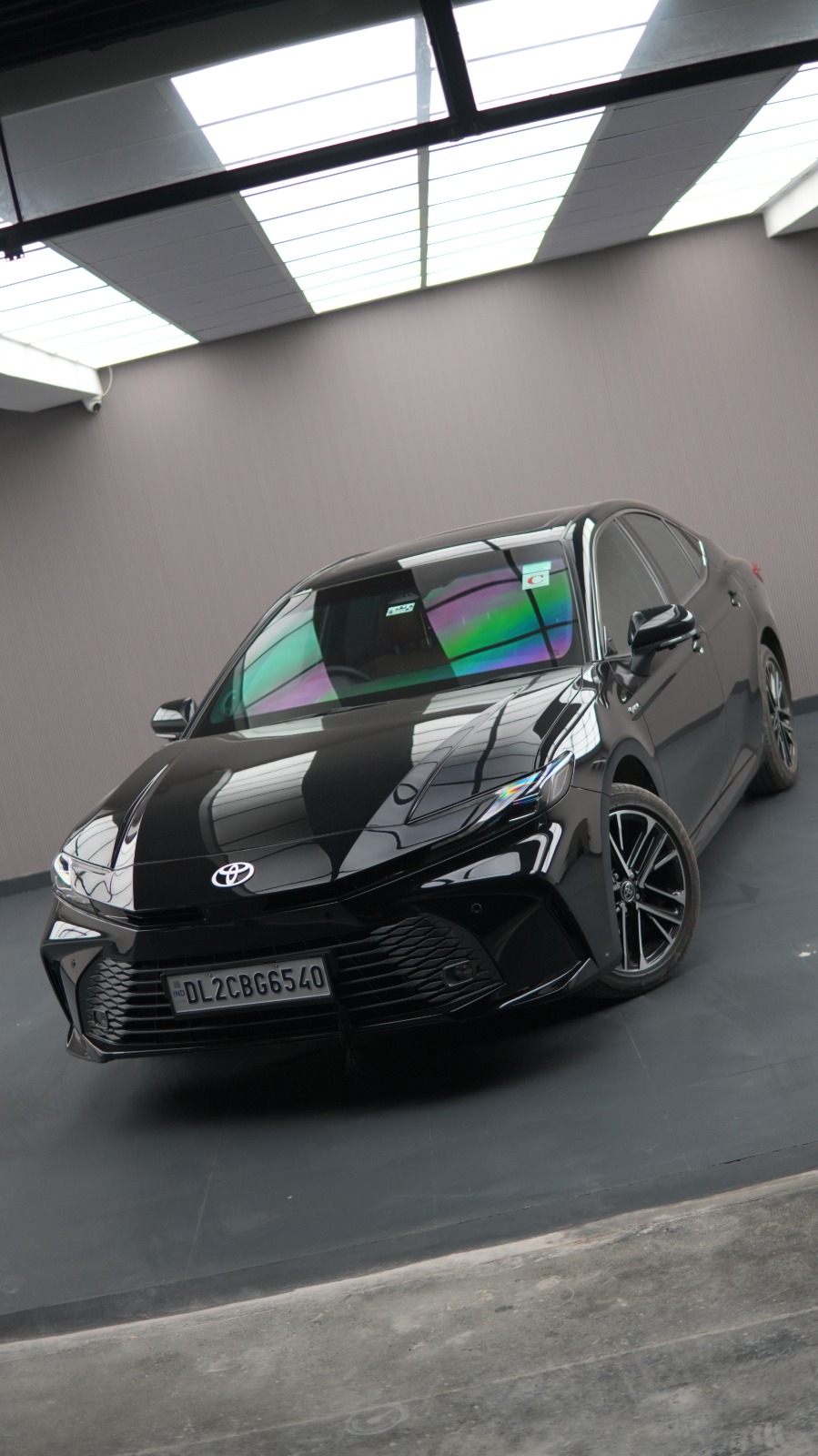 A black Toyota Camry, low front view in a white-walled bay.
