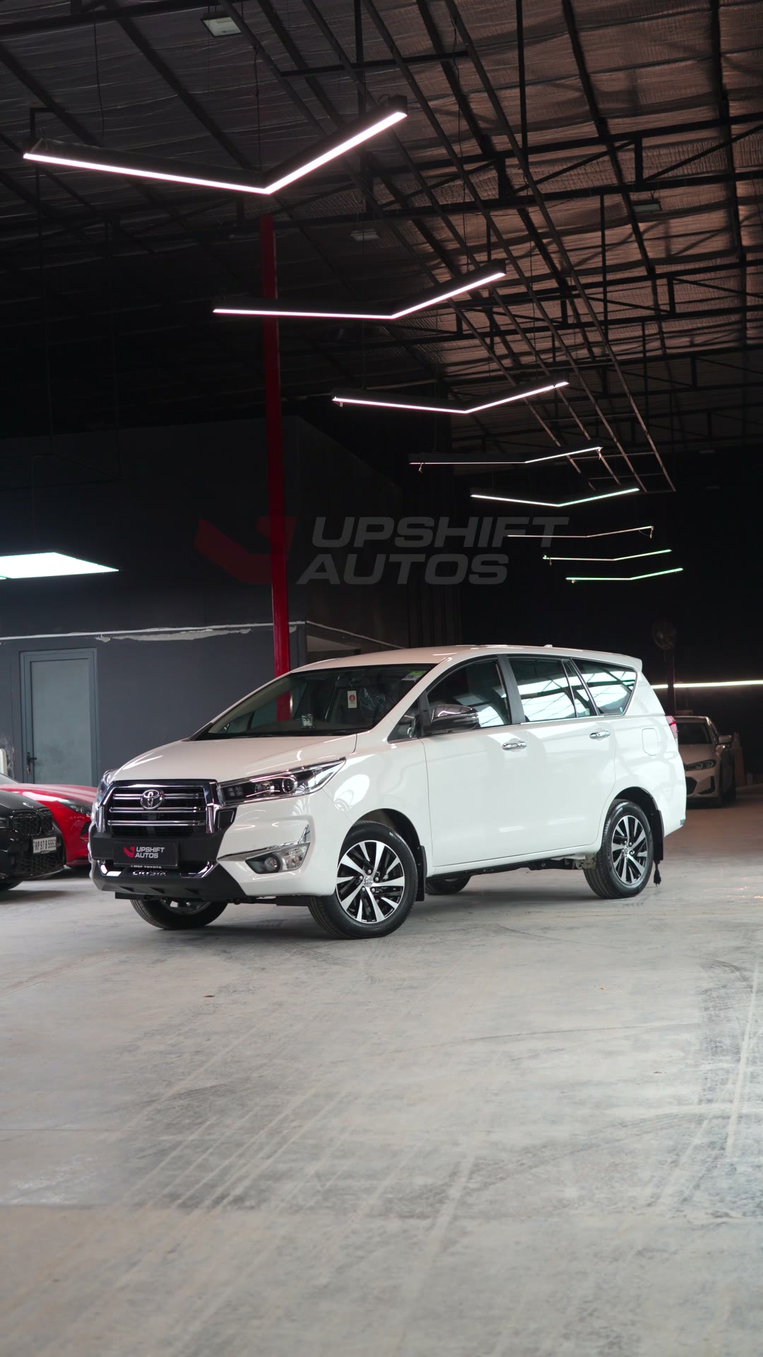 A white Toyota Innova Crysta with a chrome grille in the workshop hall, front three-quarter view.