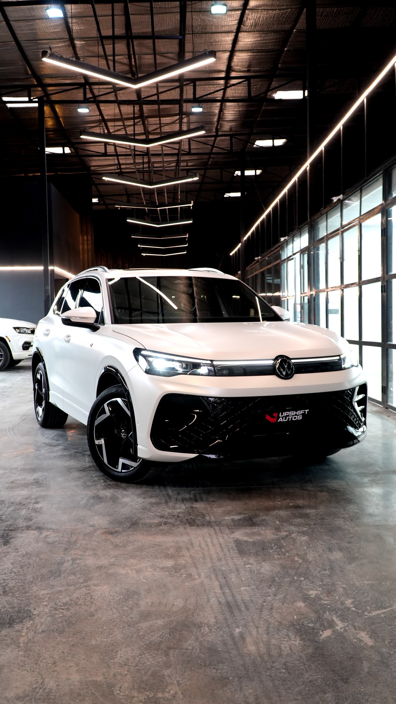 A white Volkswagen Tiguan R-Line with a lit light bar and badge, front three-quarter view in the workshop hall.